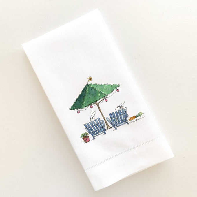 Two bunnies have a conversation sitting in Adirondack chairs beneath a topiary beach umbrella.