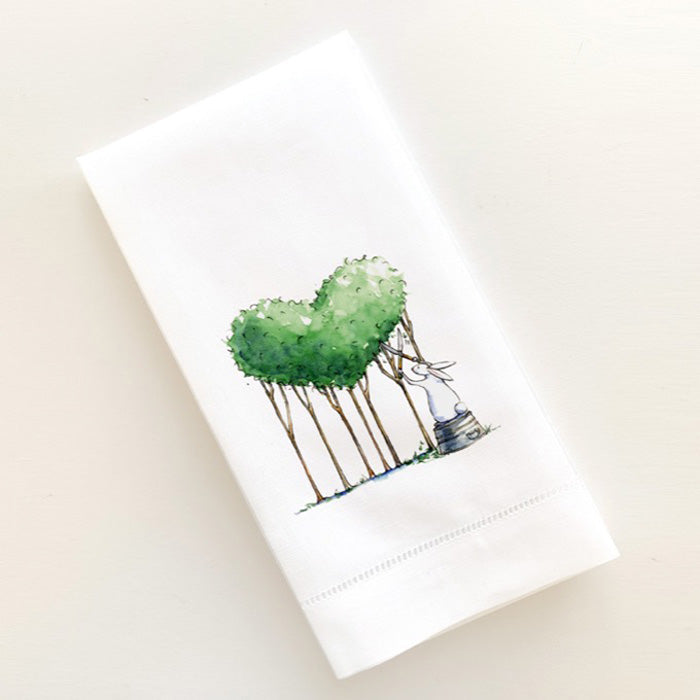 Watercolor illustration of bunny standing on pail trimming a heart made of trees printed on a linen guest towel
