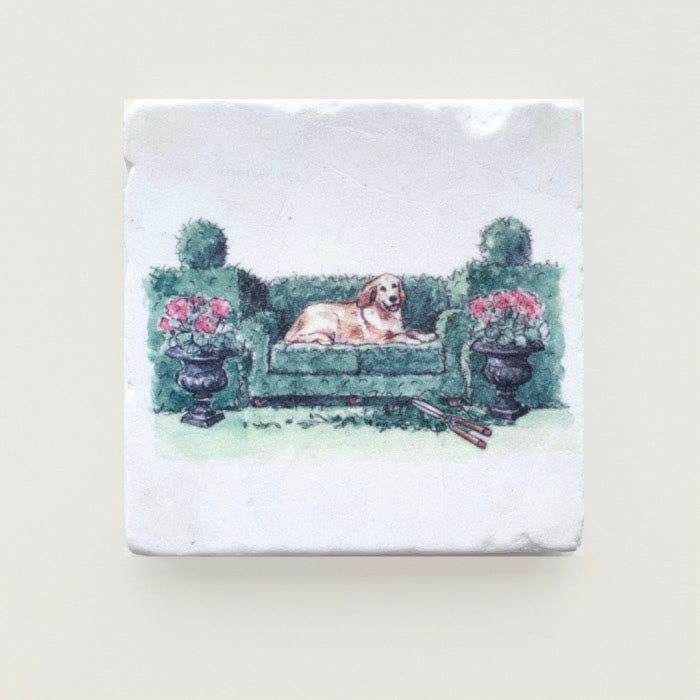 A golden retriever is lying on a topiary sofa cut out of a garden hedge. Printed by the artist on a tumbled marble coaster.